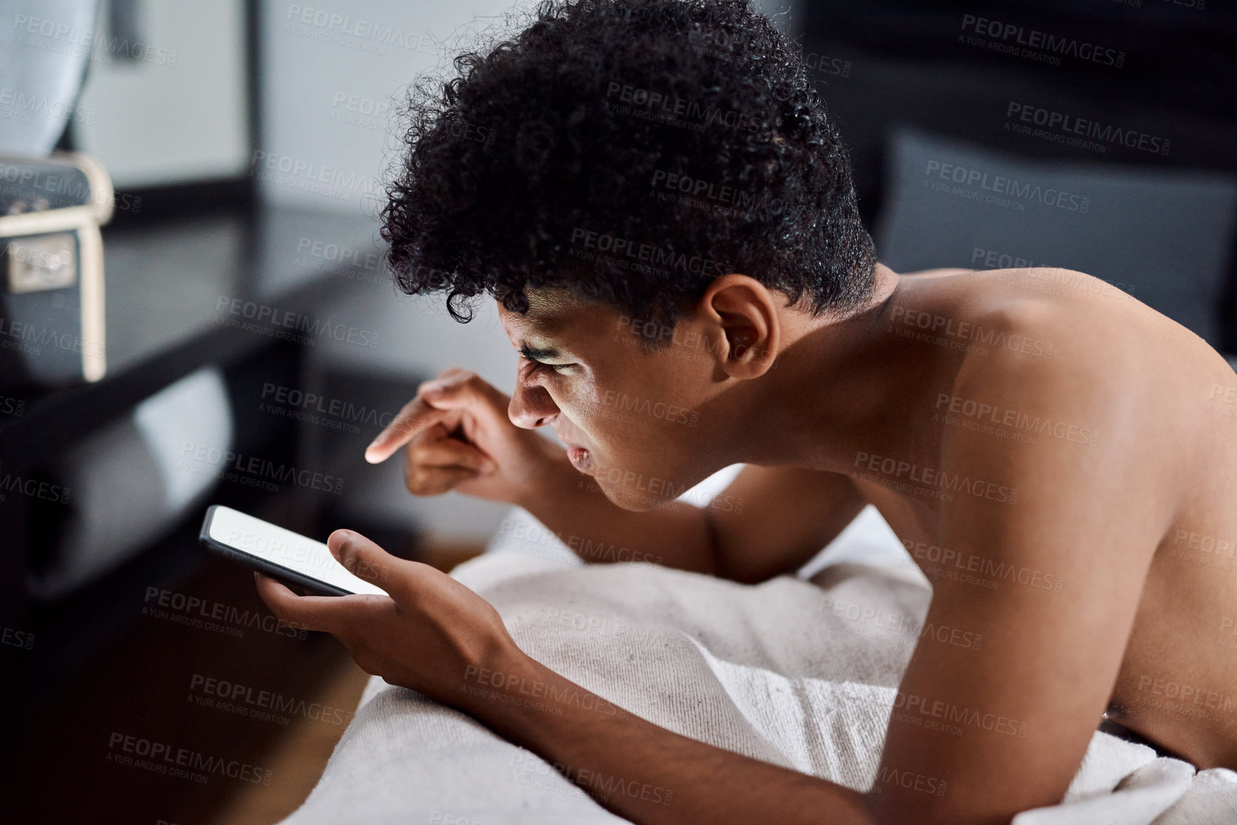 Buy stock photo Shot of a young man using a smartphone while relaxing on his bed at home