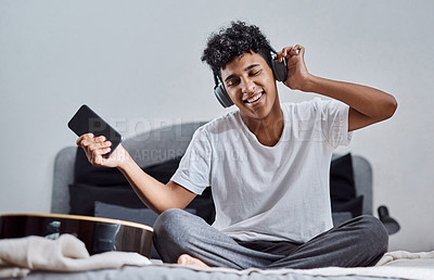 Buy stock photo Shot of a young man using a smartphone and headphones to listen to music at home