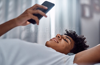 Buy stock photo Shot of a young man using a smartphone and headphones while relaxing on his bed at home