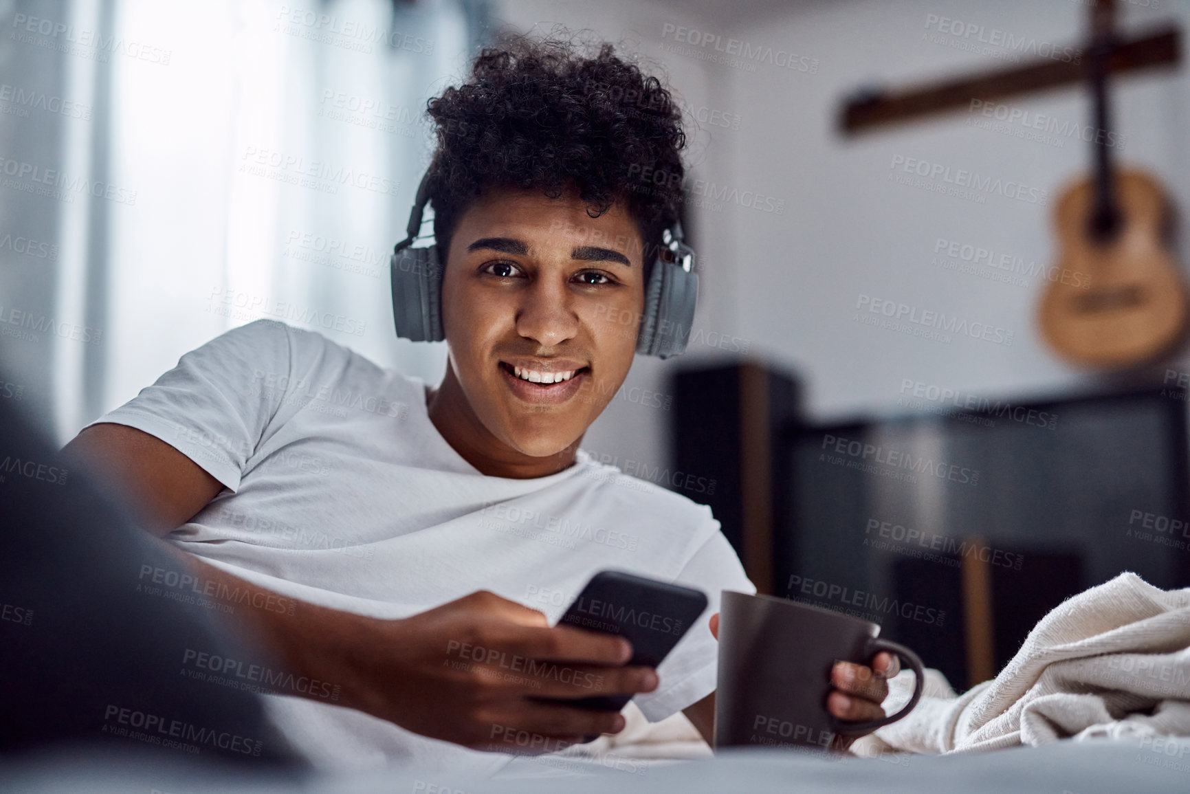 Buy stock photo Coffee, phone and portrait of happy man with headphones in bedroom, morning or scroll to relax in home. Mobile, face and person in bed with drink for streaming music, text or listen to rock in Brazil