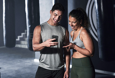 Buy stock photo Shot of two sporty people looking at something on a cellphone together in a gym