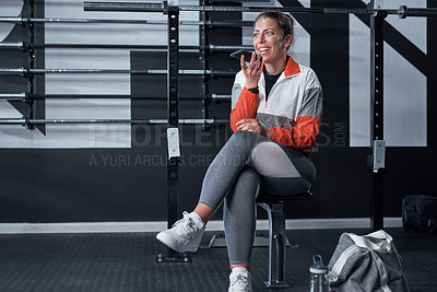 Buy stock photo Shot of a sporty young woman using a cellphone in a gym
