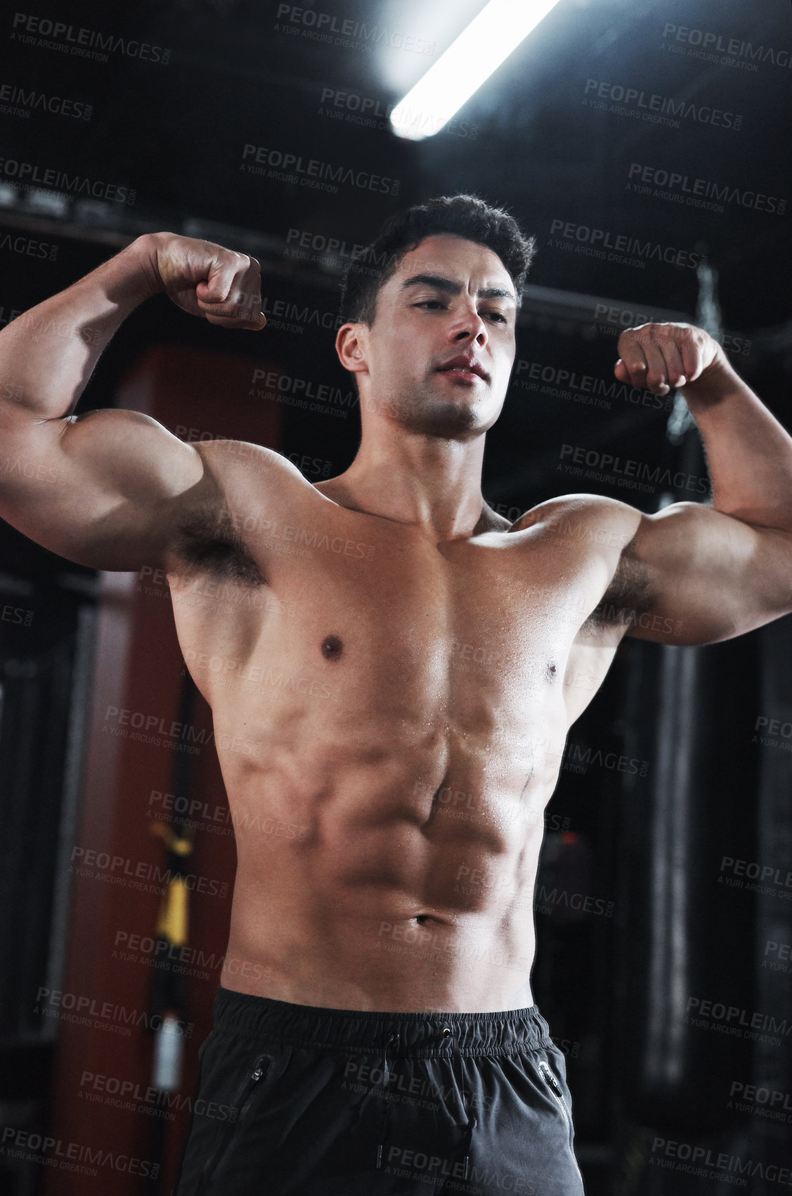 Buy stock photo Cropped shot of a handsome and buff young man flexing his biceps while shirtless in the gym
