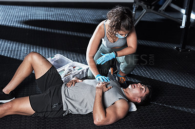 Buy stock photo Shot of a masked young woman giving an injured man first aid at the gym