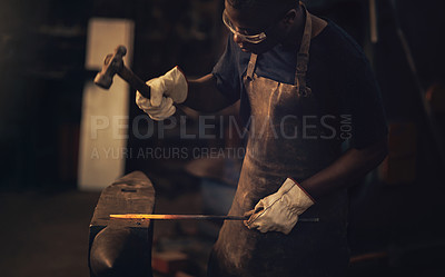 Buy stock photo Shot of a young man hitting a hot metal rod with a hammer in a foundry