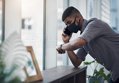 Buy stock photo Shot of a young businessman wearing a face mask and checking the time while talking on a cellphone in an office