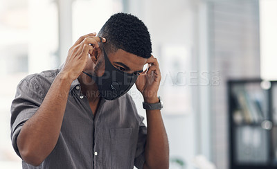Buy stock photo Shot of a young businessman putting on a face mask in an office