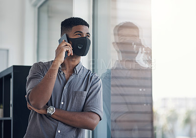 Buy stock photo Shot of a young businessman wearing a face mask while talking on a cellphone in an office