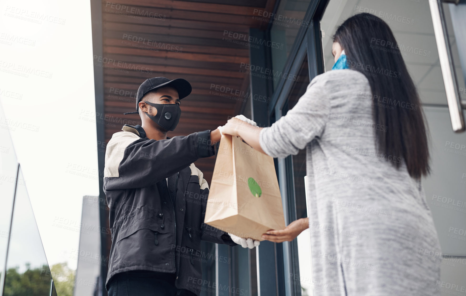 Buy stock photo Shot of a masked young woman receiving a takeout delivery at home