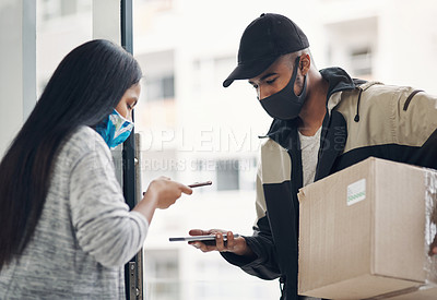 Buy stock photo Shot of a masked young man and woman using smartphones during a home delivery