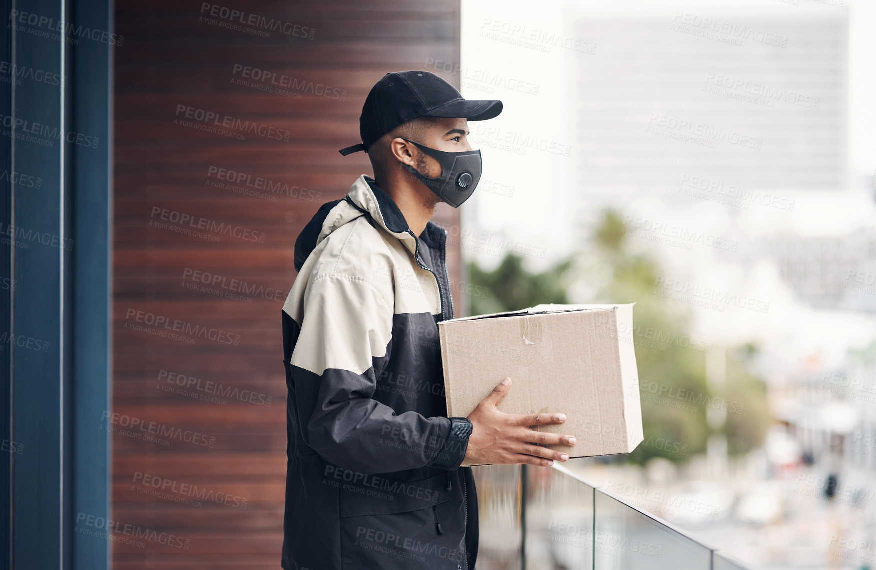 Buy stock photo Shot of a masked young man delivering a package to a place of residence