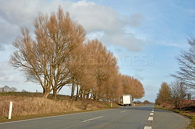 Buy stock photo Trees along a highway street with cloudy blue sky background in the countryside during autumn with copy space. Scenic landscape to admire during a road trip. Route to travel through a dry meadow 