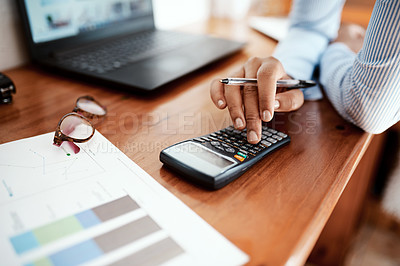 Buy stock photo Cropped shot of a businesswoman using a calculator while going over financial paperwork at her desk