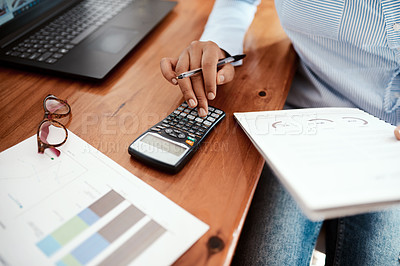 Buy stock photo Cropped shot of a businesswoman using a calculator while going over financial paperwork at her desk