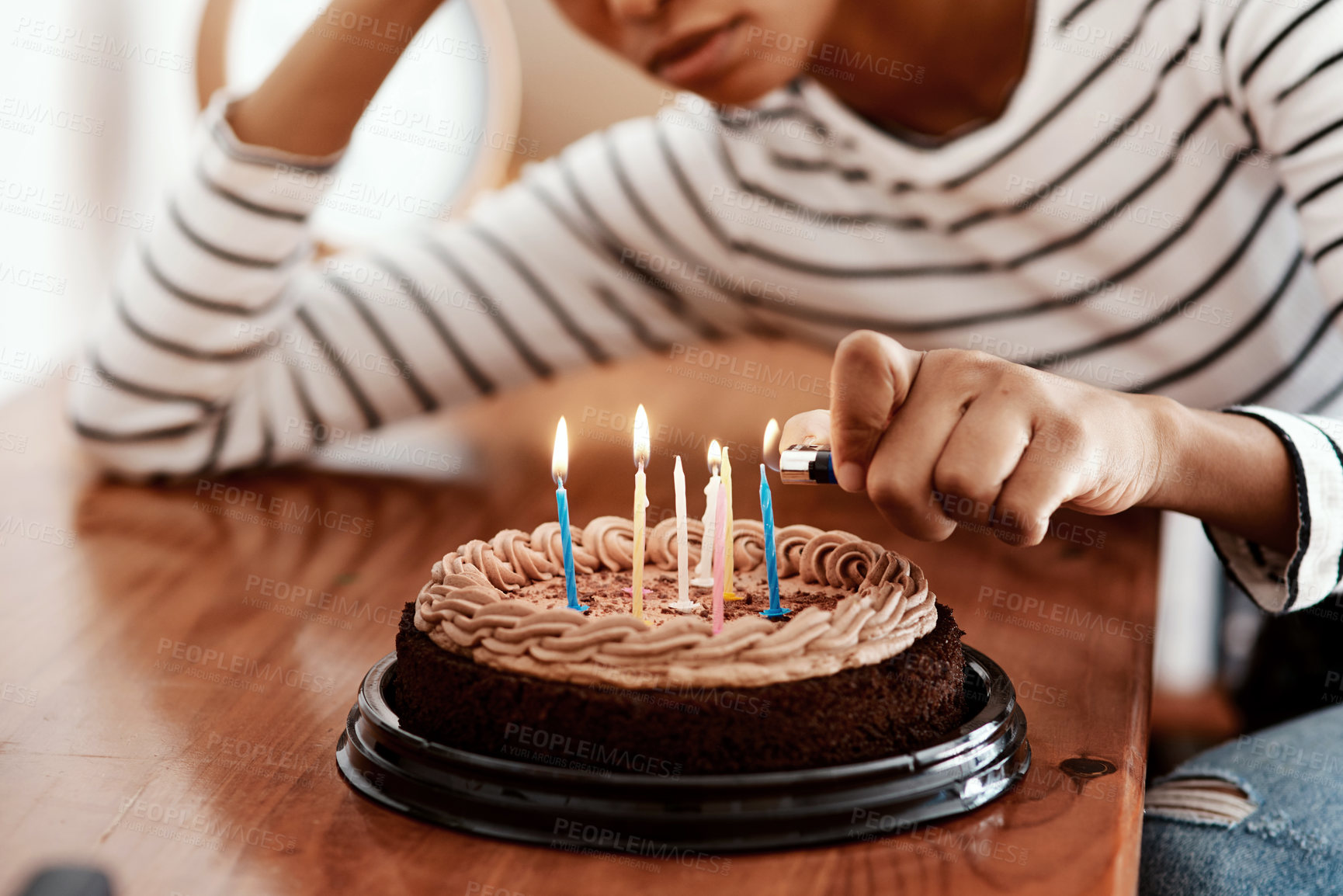 Buy stock photo Cropped shot of a woman lighting candles on a birthday cake at home and looking sad