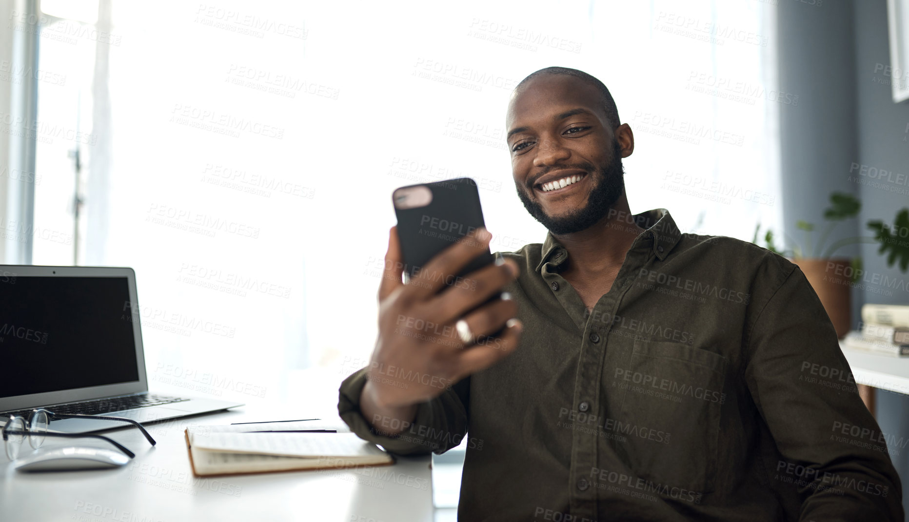 Buy stock photo Shot of a young businessman using a smartphone at his desk in a modern office