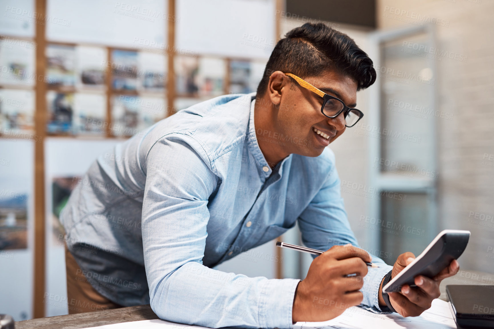 Buy stock photo Shot of a young architect using a calculator while drawing up a building plan