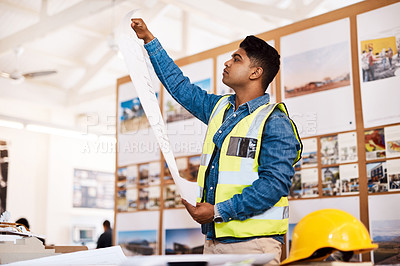Buy stock photo Shot of a young architect looking at a blueprint in his office