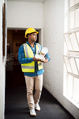 Buy stock photo Shot of a young engineer holding blueprints on a construction site