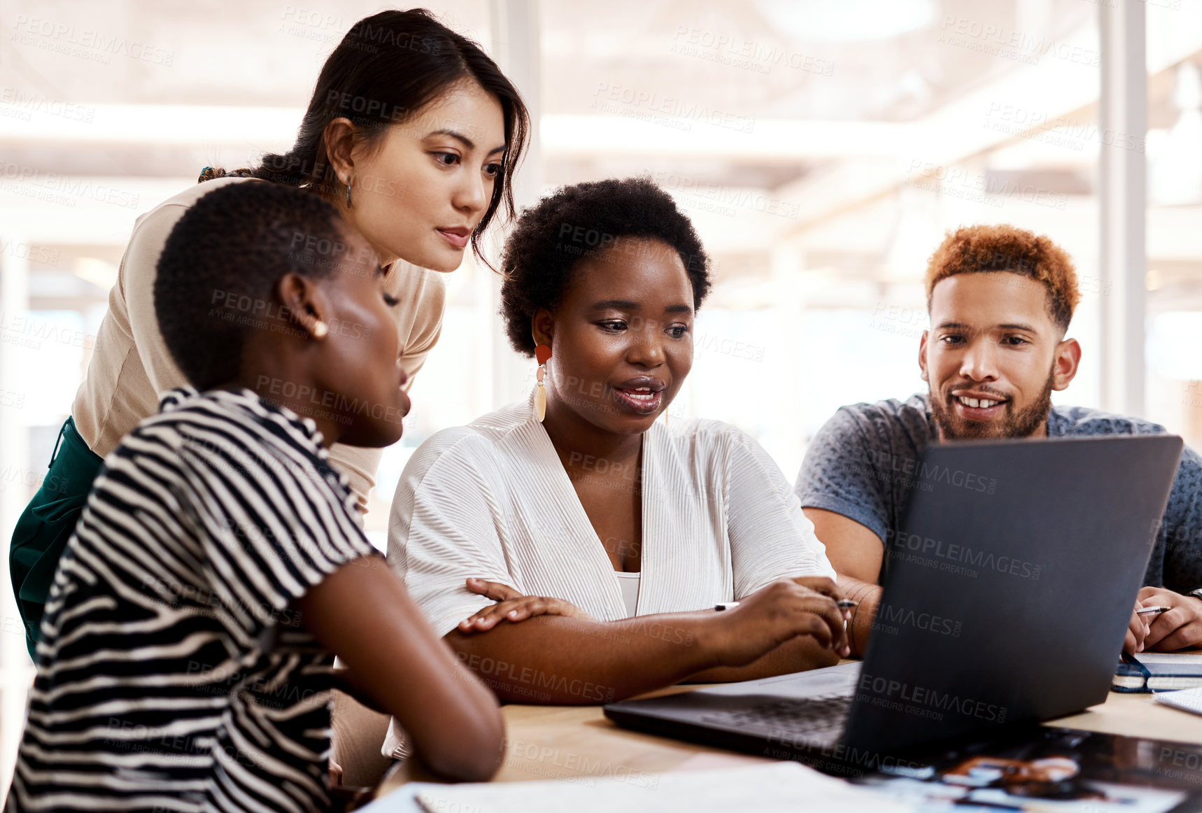 Buy stock photo Shot of a group of young creatives working together on a laptop in an office