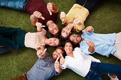 Buy stock photo Portrait of a group of young creatives showing thumbs up while lying down in a huddle together