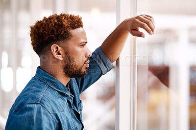 Buy stock photo Cropped shot of a handsome young male designer looking thoughtful while standing at a window in his office