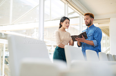 Buy stock photo Shot of two businesspeople going through a notebook together in an office