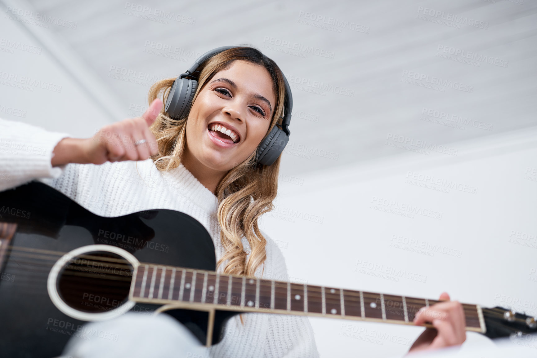 Buy stock photo Shot of a young woman wearing headphones while playing the guitar at home