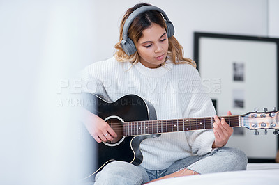 Buy stock photo Shot of a young woman wearing headphones while playing the guitar at home