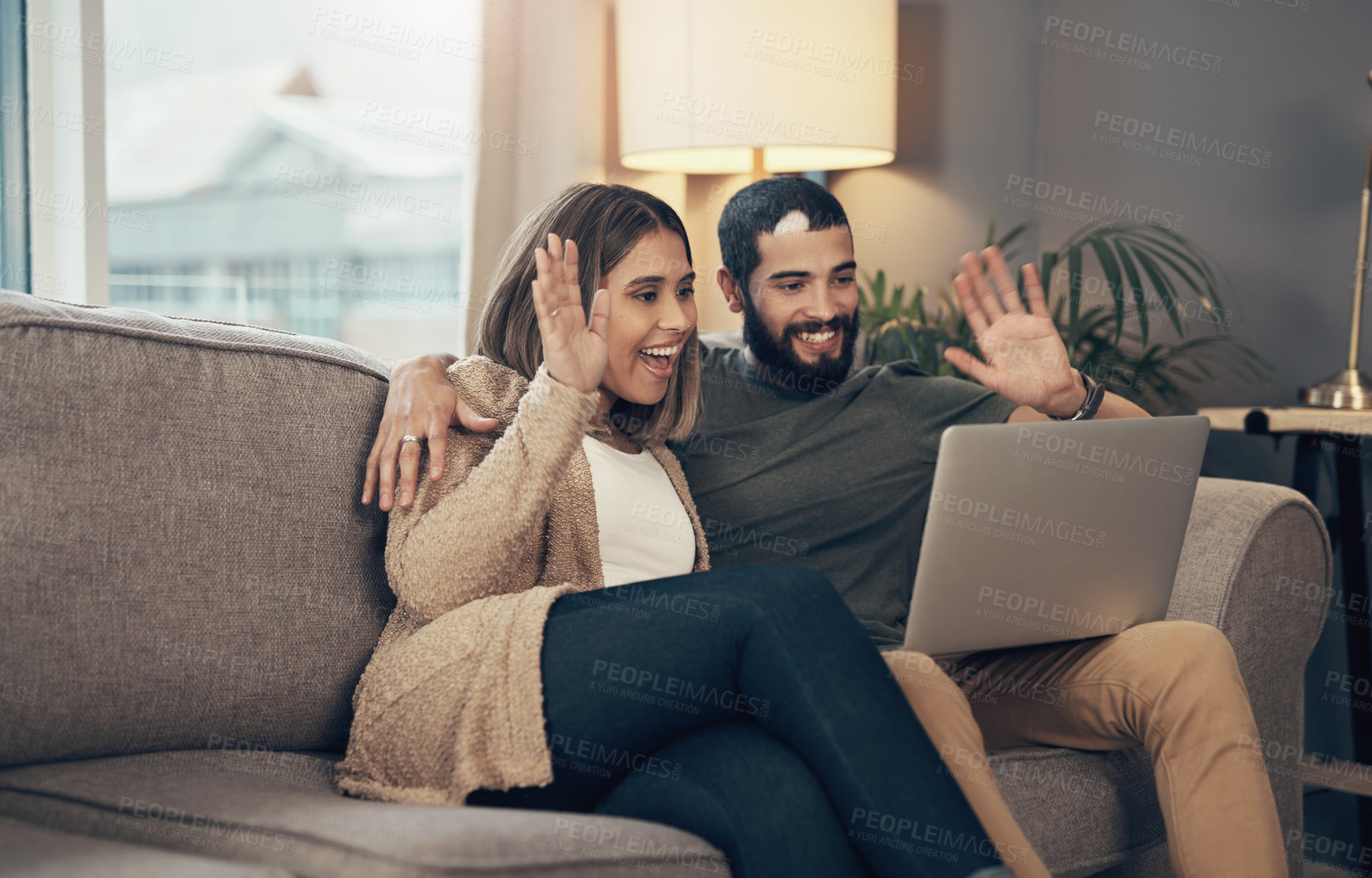 Buy stock photo Shot of a young couple using a laptop to make a video call on the sofa at home
