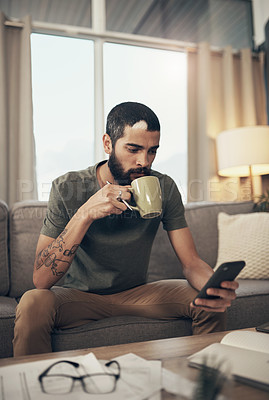 Buy stock photo Shot of a young man having coffee and using a smartphone while going through paperwork at home