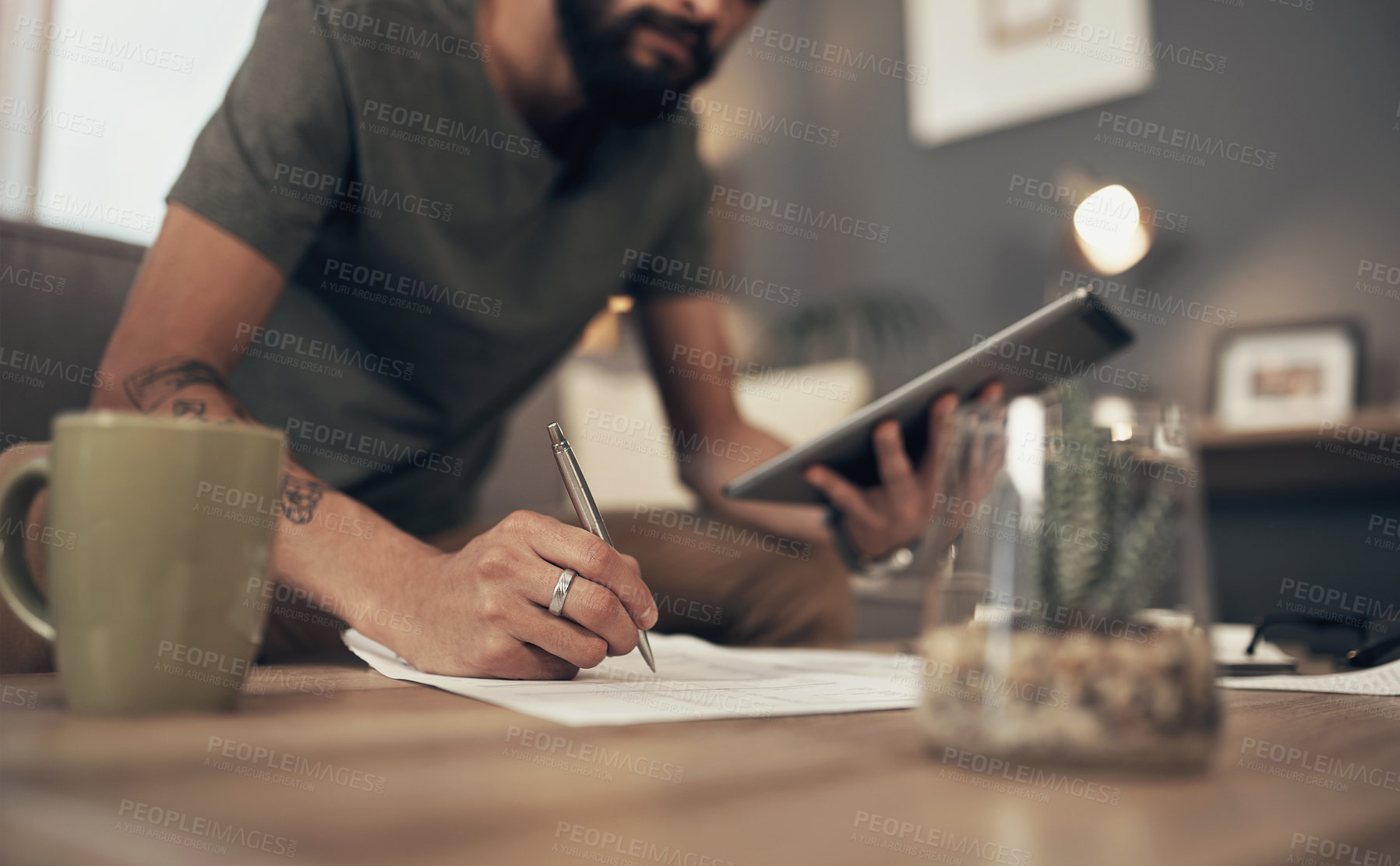 Buy stock photo Cropped shot of a man using a digital tablet while going through paperwork at home