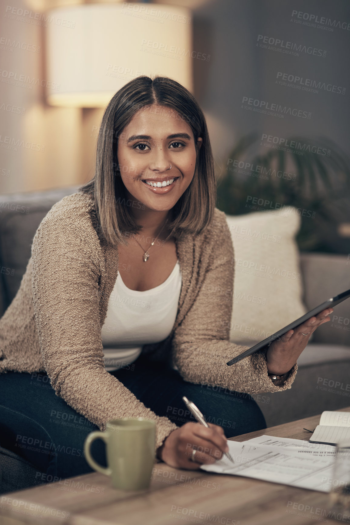 Buy stock photo Shot of a young woman using a digital tablet while going through paperwork at home