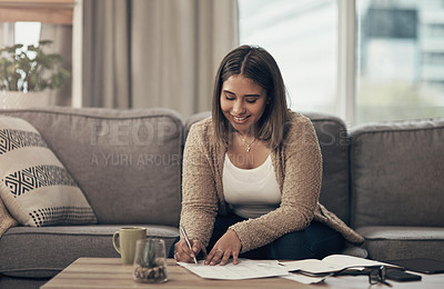 Buy stock photo Shot of a young woman going over paperwork at home