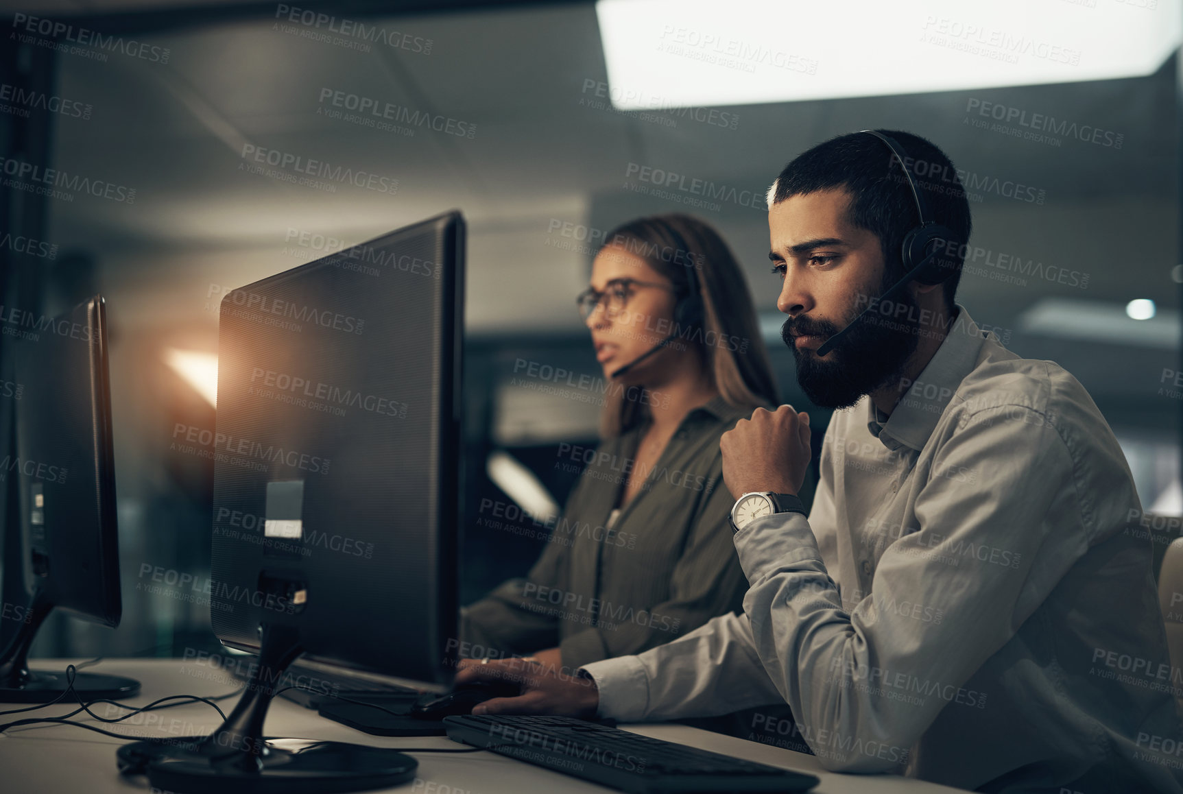 Buy stock photo Shot of a call centre agent working in an office alongside a colleague at night