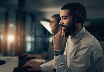 Buy stock photo Shot of a call centre agent working in an office alongside a colleague at night