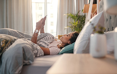 Buy stock photo Shot of a young woman using a cellphone while lying in bed at home