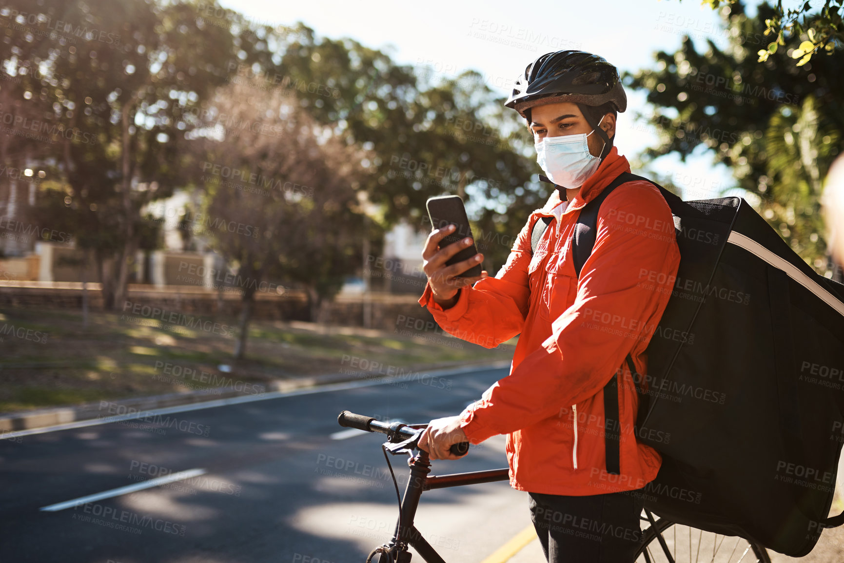 Buy stock photo Shot of a masked man using his cellphone while out on his bicycle for a delivery