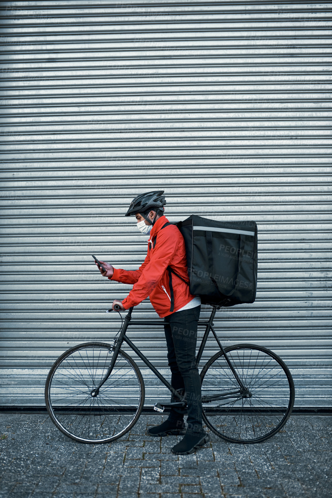Buy stock photo Shot of a masked man using his cellphone while out on his bicycle for a delivery