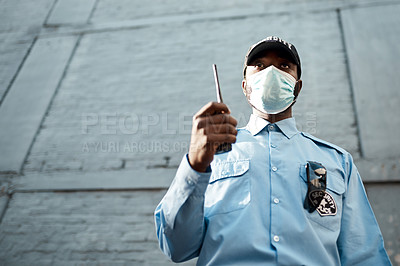Buy stock photo Shot of a masked young security guard using a two way radio while on patrol outdoors