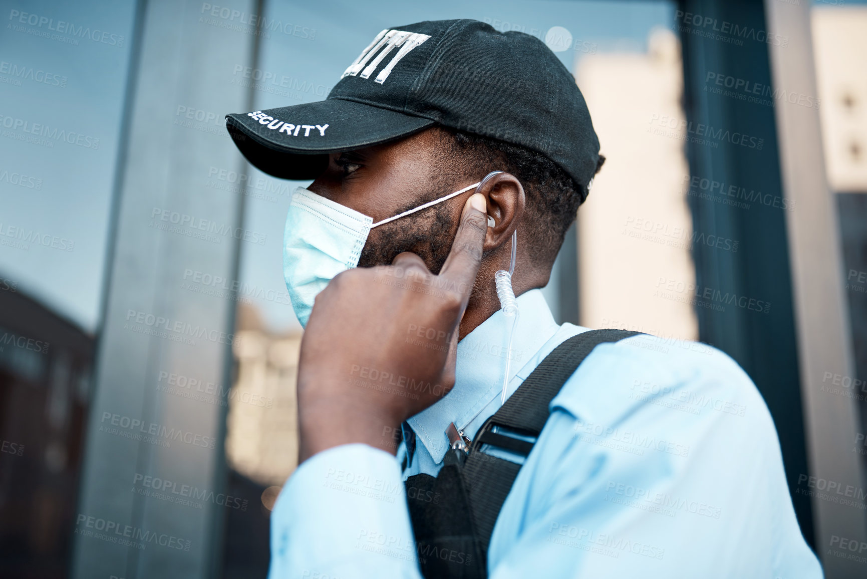 Buy stock photo Shot of a masked young security guard using an earpiece while on patrol outdoors