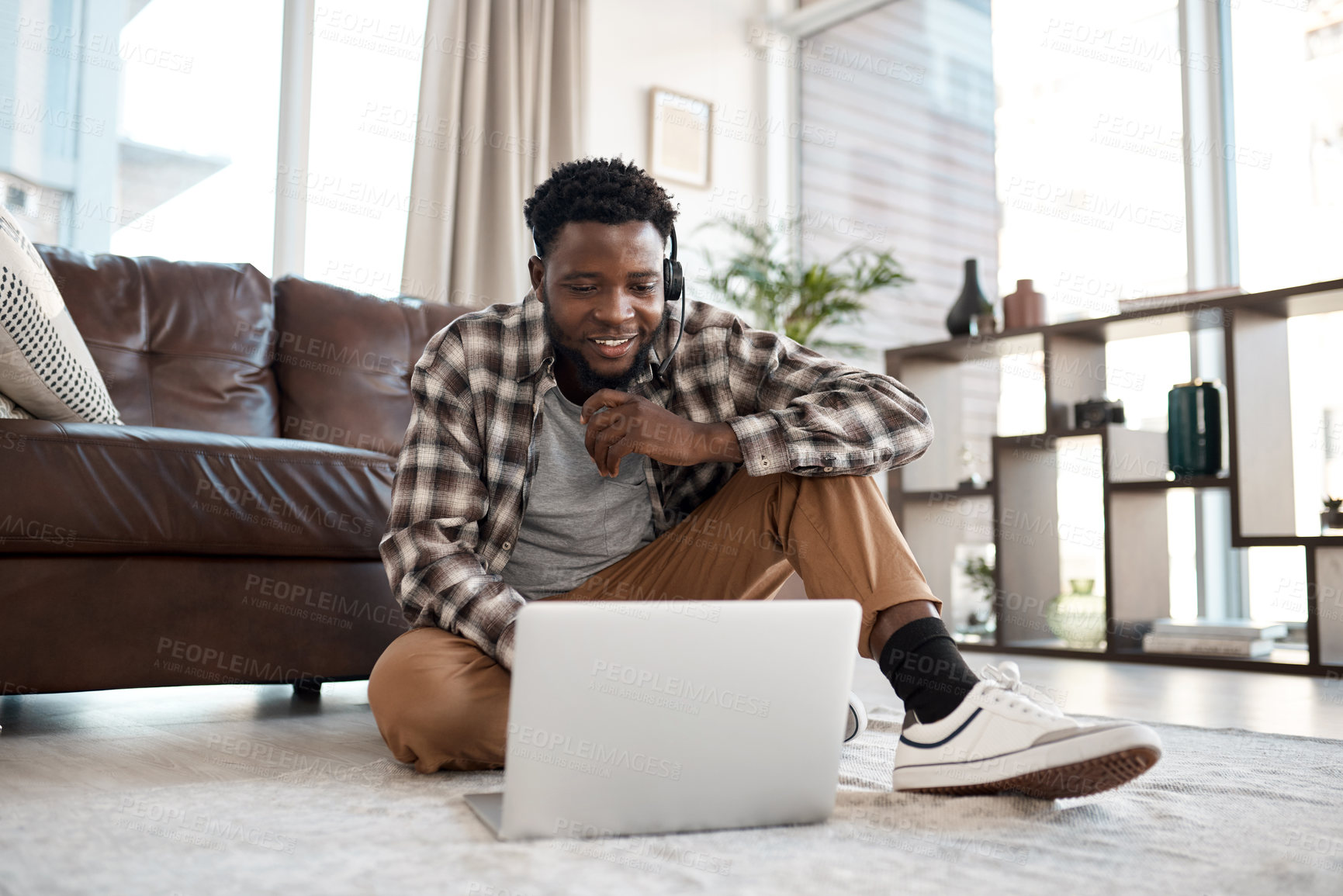 Buy stock photo Shot of a young man wearing a headset while working on a laptop at home