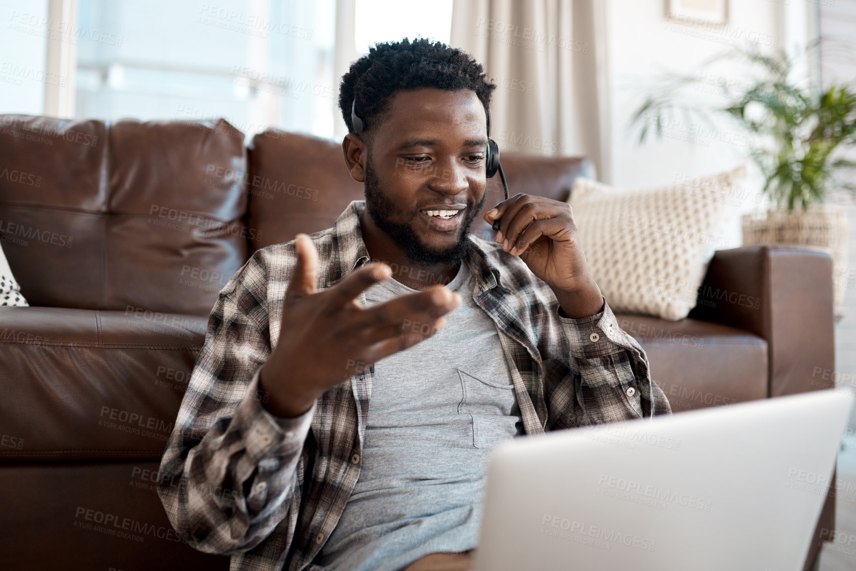 Buy stock photo Shot of a young man wearing a headset while working on a laptop at home