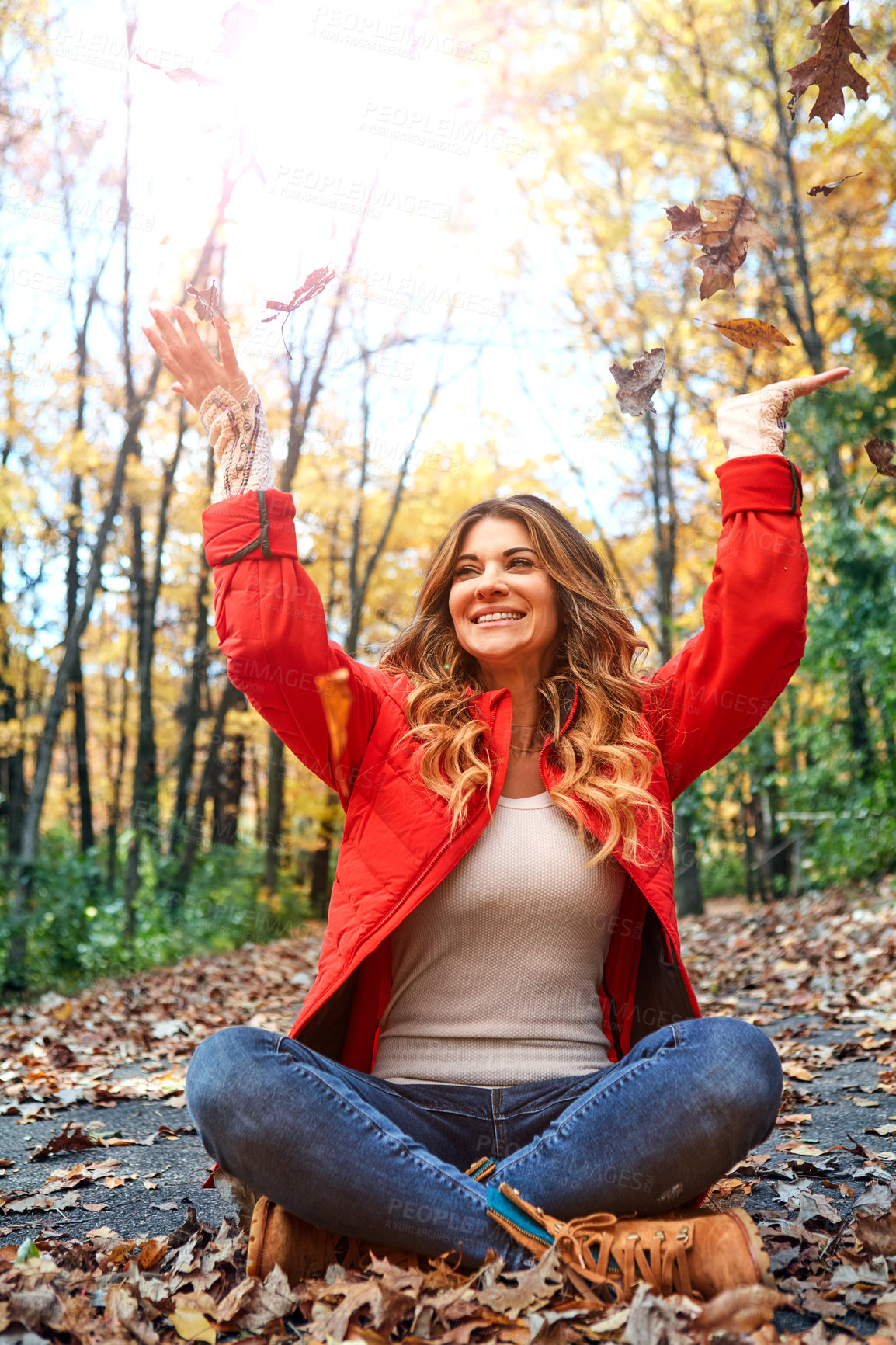 Buy stock photo Full length shot of an attractive young woman throwing leaves while sitting in the forest during autumn