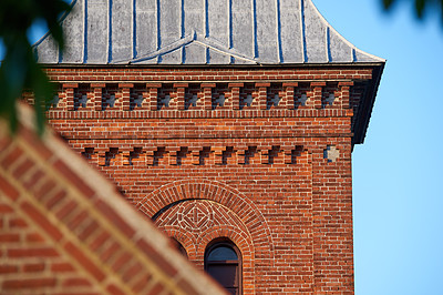 Buy stock photo Closeup of a red face brick church steeple against a blue sky. Tall infrastructure and tower used to symbolise faith and Christian or Catholic devotion. Architecture of a built structure outside