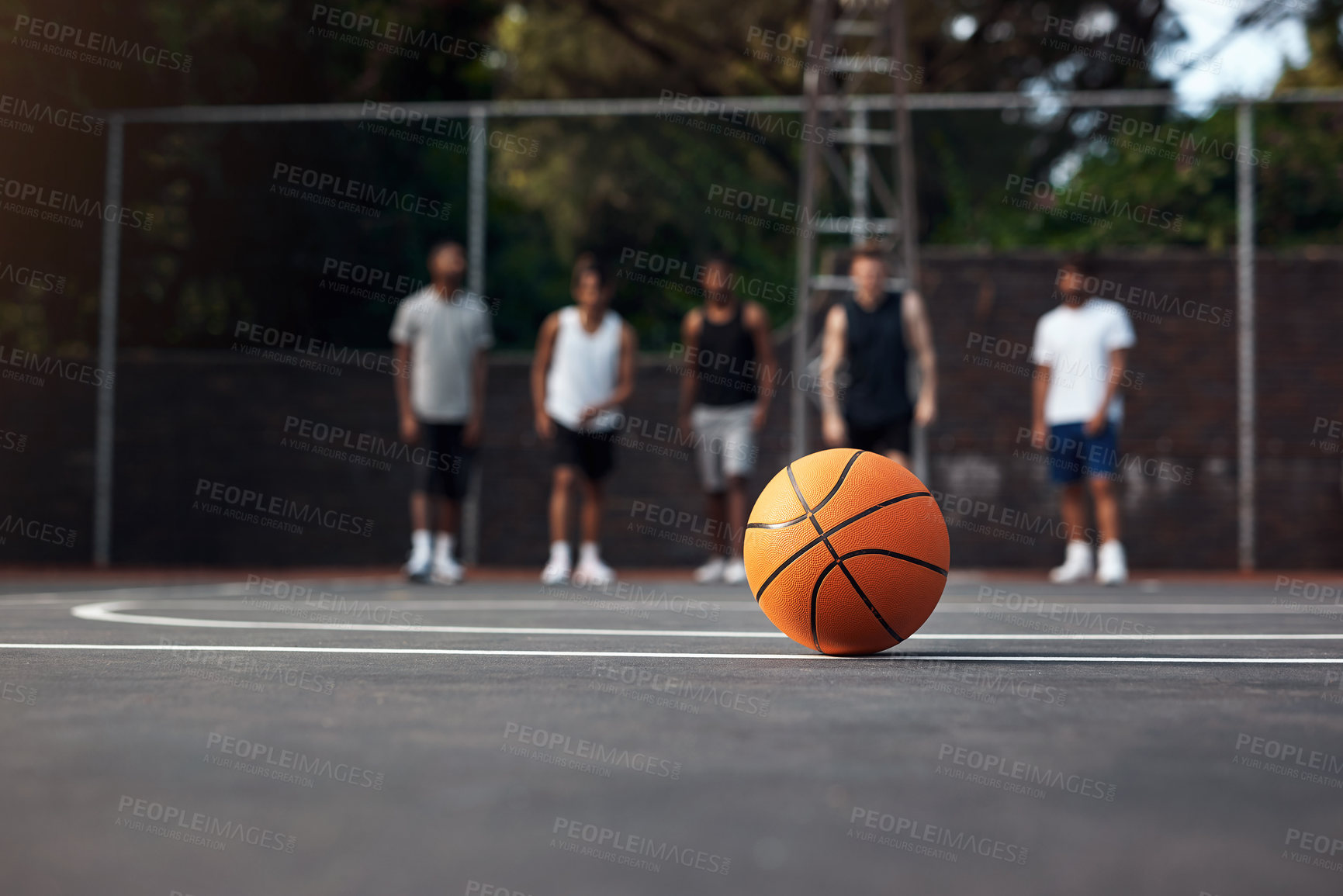 Buy stock photo Closeup shot of a basketball on a sports court with a group of young men in the background