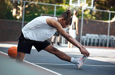 Buy stock photo Shot of a sporty young man stretching his legs on a basketball court