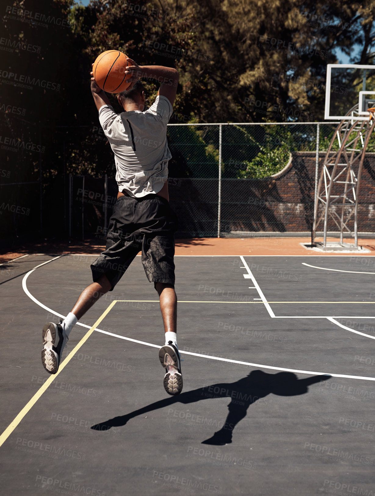 Buy stock photo Rearview shot of a sporty young man throwing a basketball into a net on a sports court