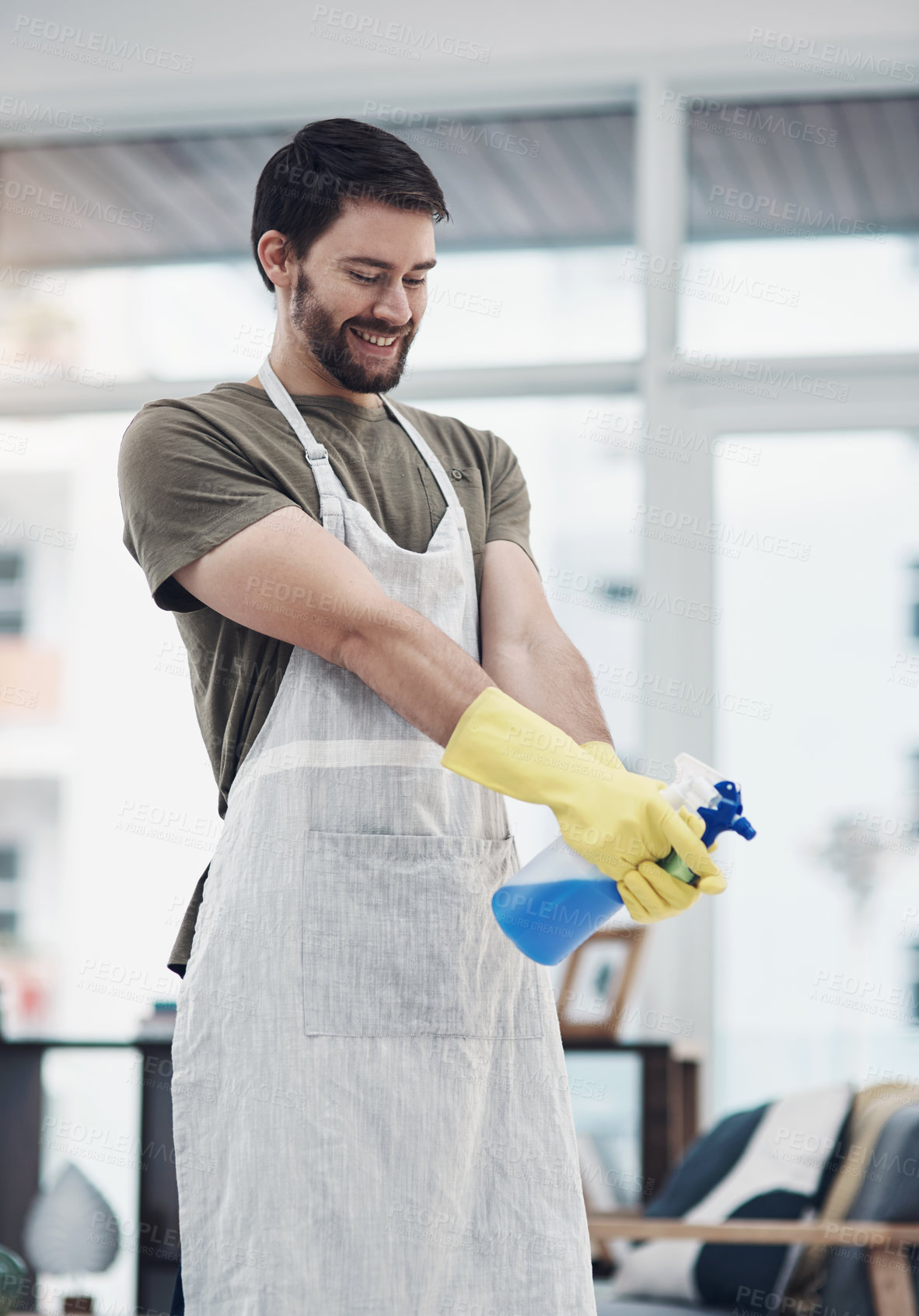 Buy stock photo Shot of a young man using rubber gloves and disinfectant to clean his home