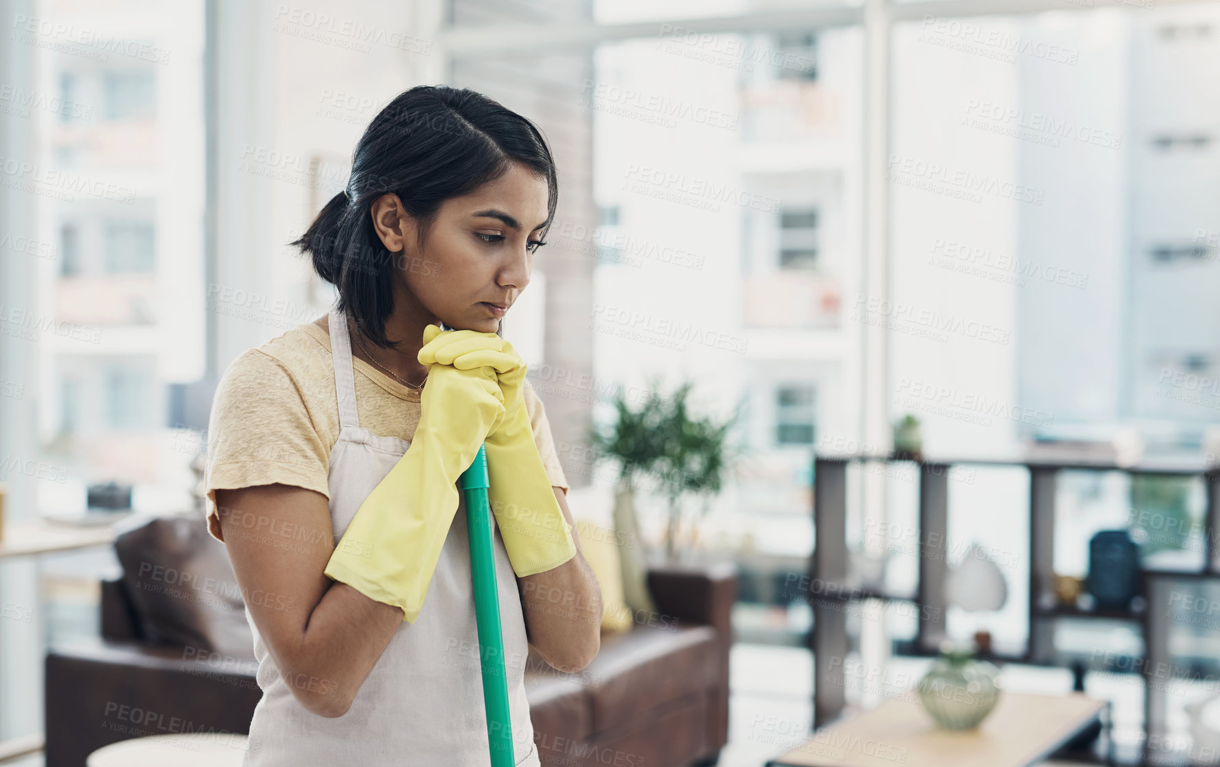 Buy stock photo Shot of a young woman looking unhappy while cleaning her home
